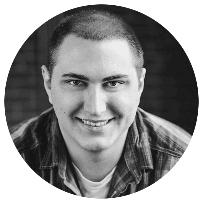 A person with short hair and a plaid shirt smiling in a black and white close-up portrait, against a blurred background.