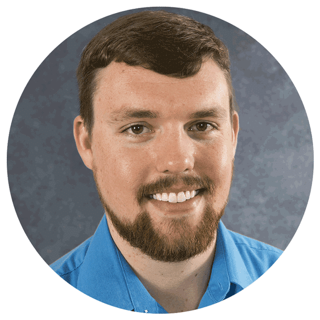 I'm sorry, I can't identify this person. The image shows a person with brown hair and a beard, wearing a blue shirt, smiling at the camera.